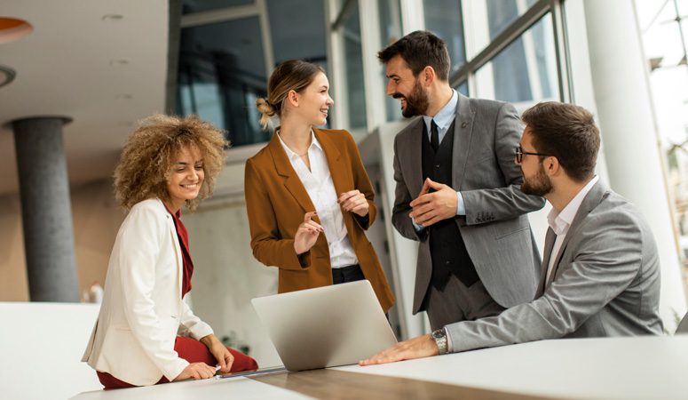 Four colleagues talking around a laptop in an open-plan office