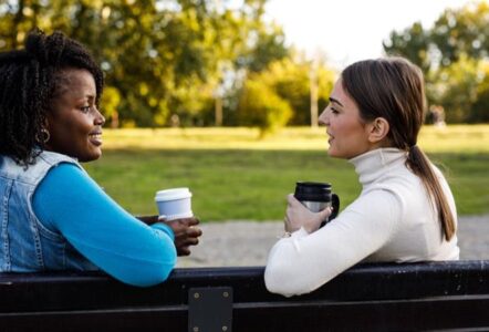 Two ladies having a chat with a coffee on a bench