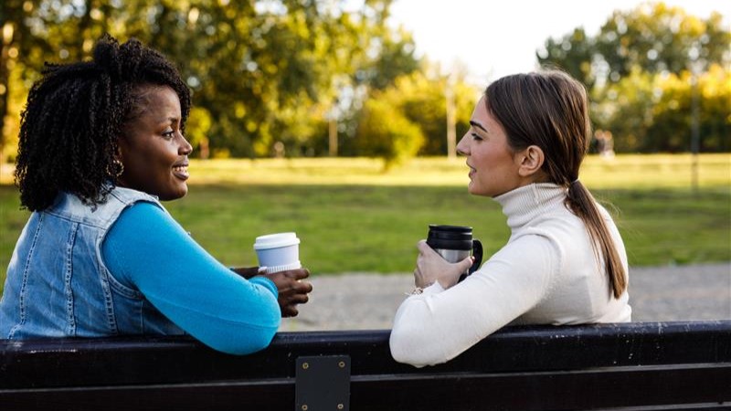 Two ladies having a chat with a coffee on a bench