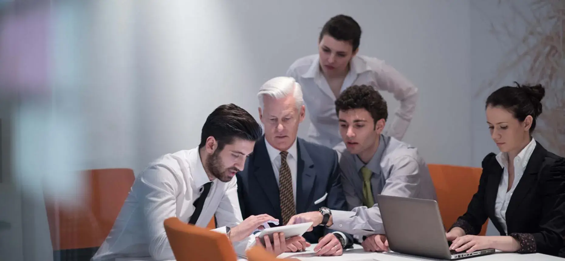 4 employees looking at tablet while fifth employee types on laptop