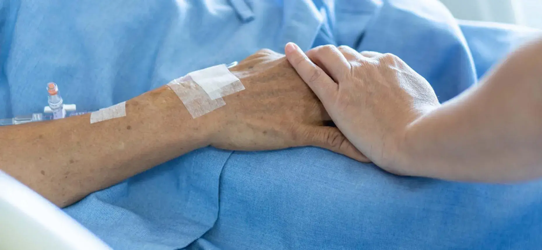person holding hands with patient in hospital bed