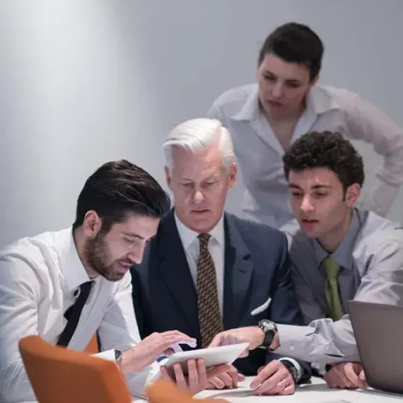 4 employees looking at tablet while fifth employee types on laptop