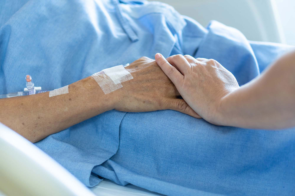 person holding hands with patient in hospital bed